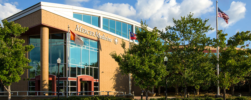 A brick and glass building with a flag out front with a Mercer Medicine sign above the door